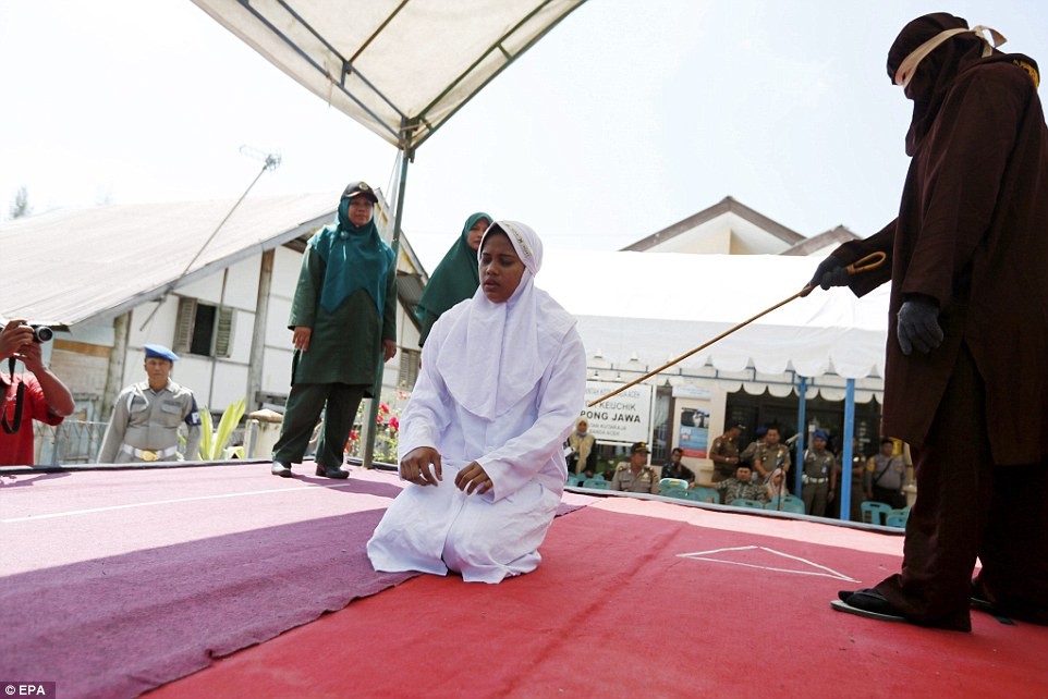 Một  cặp đôi ngoại tình ở Indonesia đã phải chịu hình phạt hà khắc theo Luật Hồi giáo Sharia trước sự chứng kiến của đông đảo người dân. Ảnh: Cô gái Indonesia trót quan hệ ngoài luồng đang quỳ trên khu vực thi hành án phạt ở tỉnh Aceh. Ảnh Daily Mail